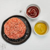 Raw ground beef sprinkled with salt and pepper accompanied by ketchup and mustard
